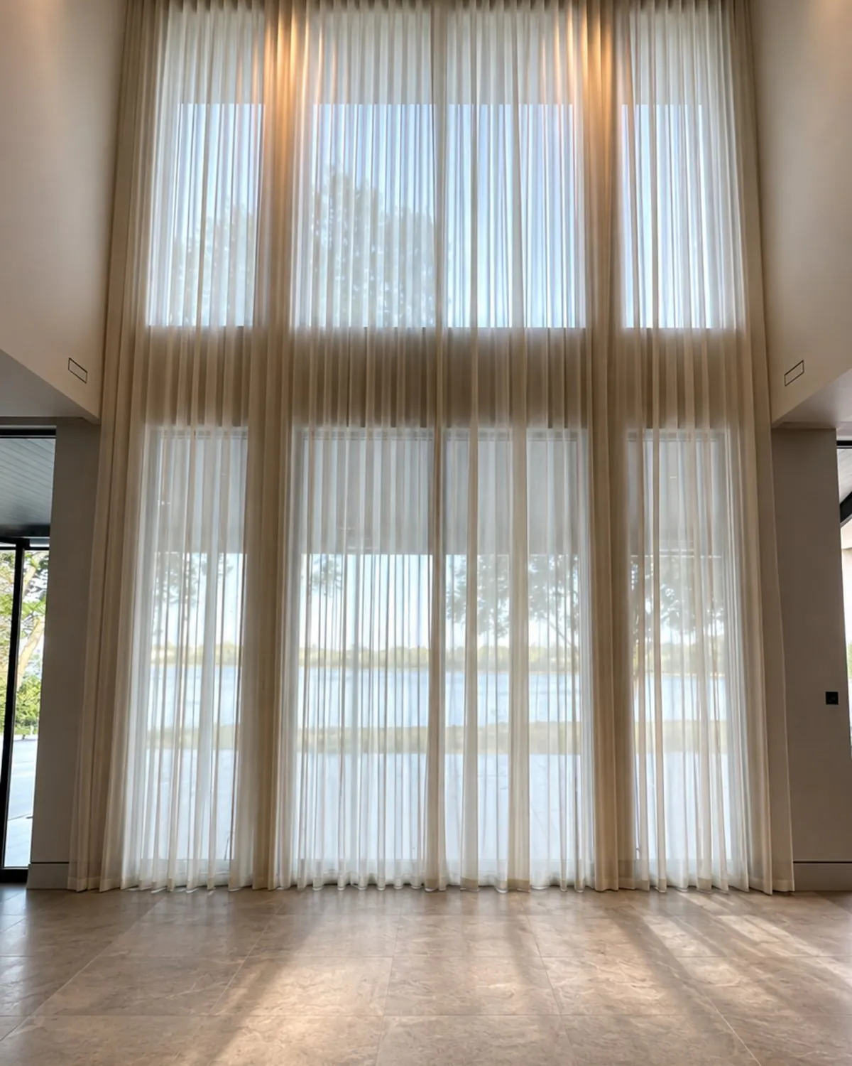 Floor-to-ceiling sheer curtains on a ceiling track across a wall of glass