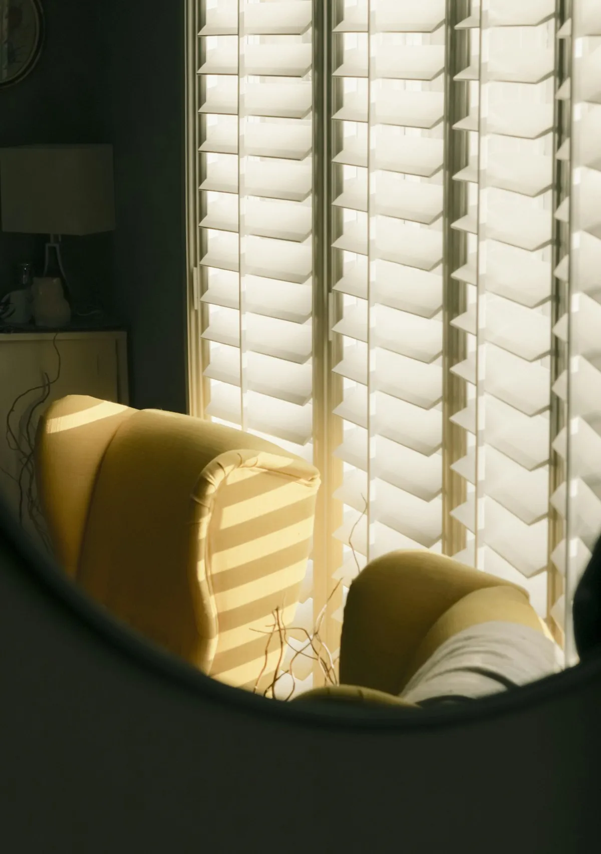 White plantation shutters with sunlight through the louvers beside an armchair