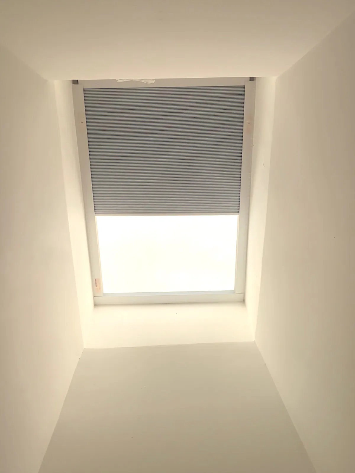 A cellular skylight shade half-drawn across a ceiling skylight